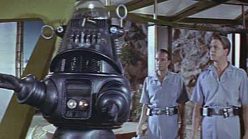 Film still of a large rounded robot standing beside two uniformed crew members in a room.